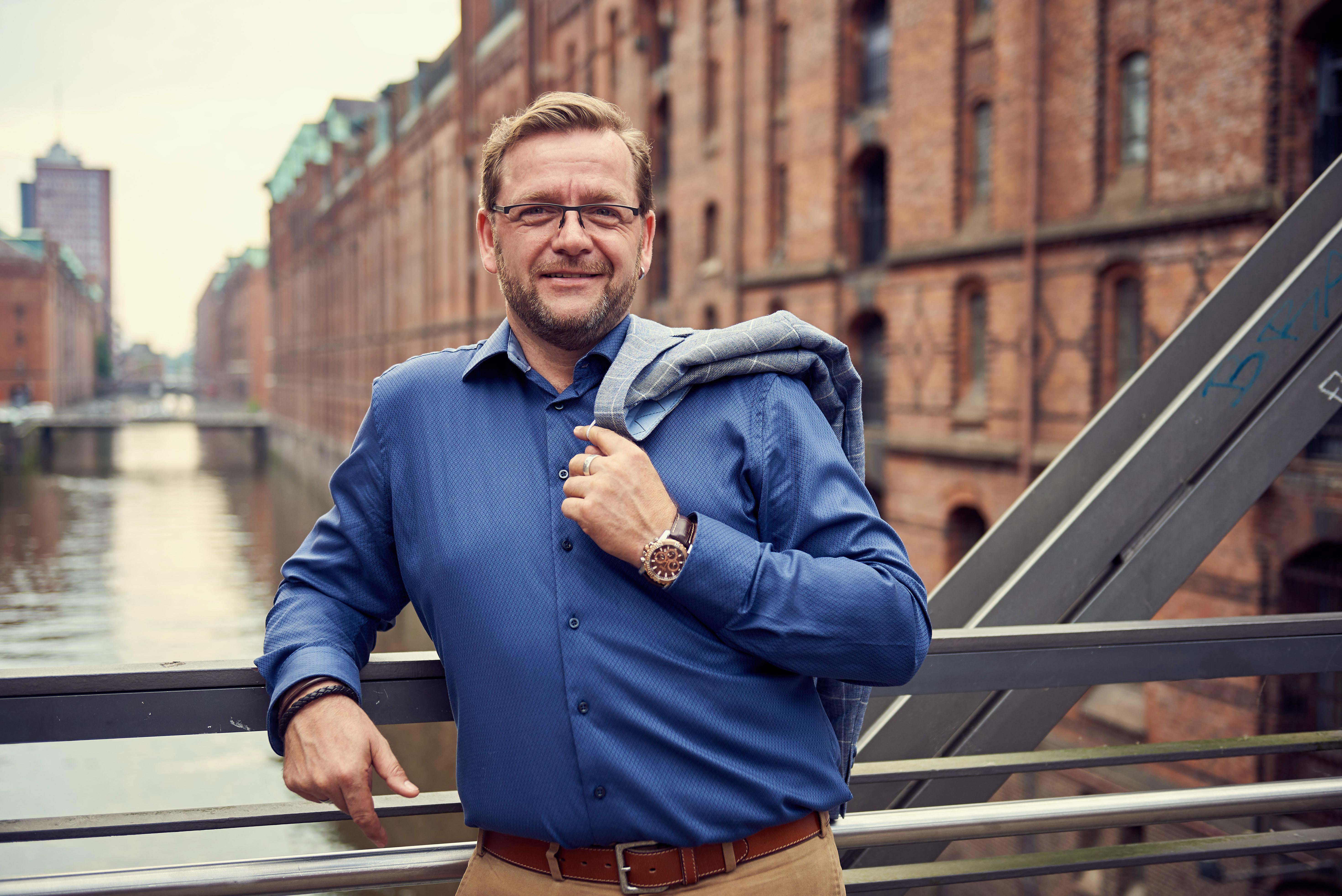 Hypnose-Therapeut wirft Sakko auf einer Brücke in der Hamburger Speicherstadt über die Schulter